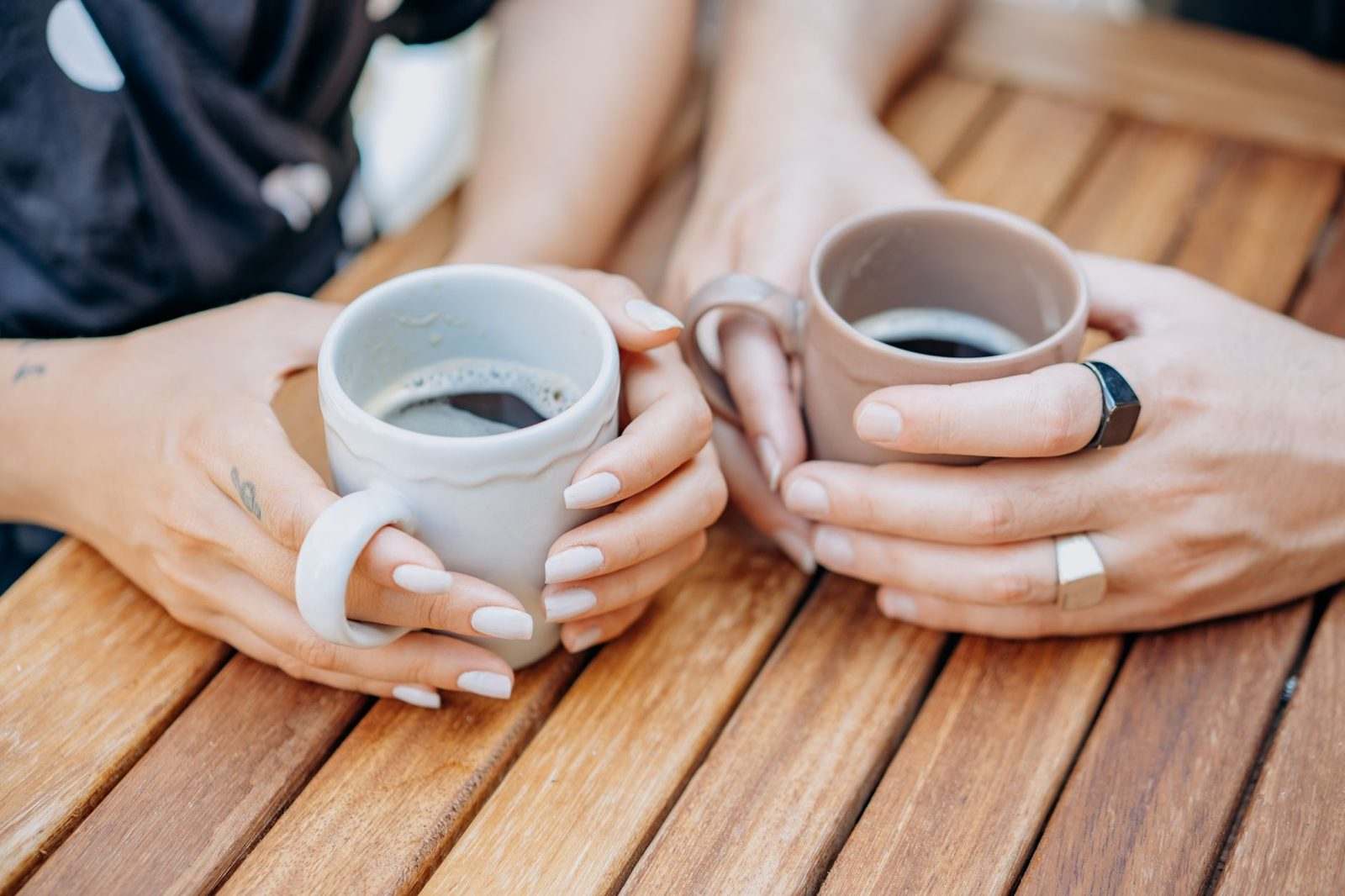 Two people cradling cups of coffee at a wooden table